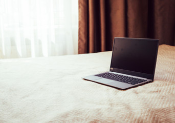 New laptop with blank screen on bed blanket in home bedroom interior
