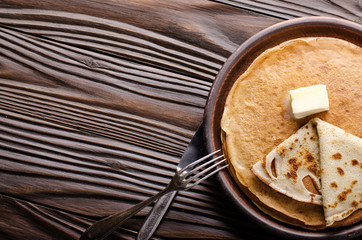 Flat lay view at Stack of French crepes with butter in ceramic dish on wooden kitchen table