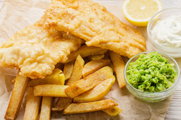 Traditional British street food fish and chips with tartar sauce and mushy peas on paper plate