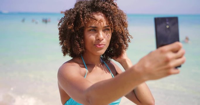 Cheerful ethnic woman taking selfie on beach
