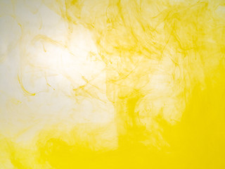 Clouds of acrilic paint swirling in water, close up view. Blurred background. Drop of yellow ink...