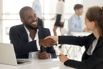 Fototapeta na wymiar Happy african manager broker handshaking caucasian client at meeting