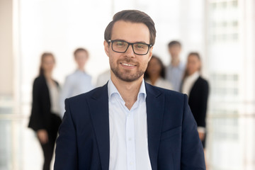 Confident businessman manager looking at camera with team on background