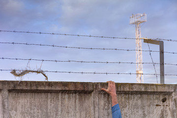Fototapeta premium Escape from jail. Prison wall with barbed wire and a watchtower on blue sky background.