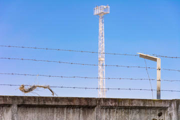 Fototapeta premium Concrete wall, against the backdrop of barbed wire, the concept of prison, salvation, refugee, lonely. Barbed wire fence detail. Silhouette barbed wire and a watchtower