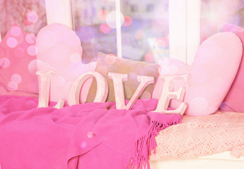 Wooden letters of the word Love. four letters make up the word Love stand against the light from the window and bokeh. Blankets, pillows, soft, light, comfort, warmth up the atmosphere of love.
