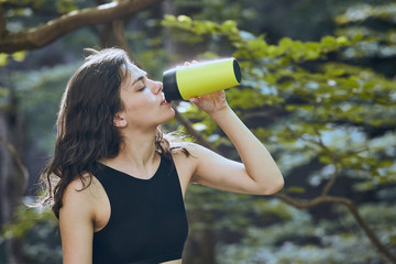 Healthy fitness girl drinking water from green bottle in forest