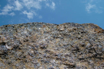 Rock or stone on blue sky with clouds background. Granite crouan rim or pick edge like cliff or mountain. Geology mineral texture closeup on two thirds