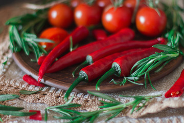 Fresh cherry tomatoes, sprigs of rosemary and chili peppers on a clay plate on the table. Fresh vegetables, herbs, and spices - healthy eating   - Image