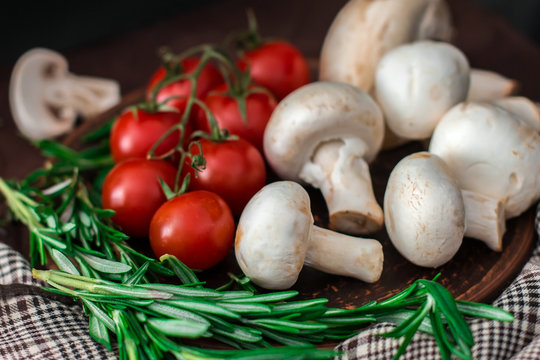 Fresh cherry tomatoes, sprigs of rosemary and champignon mushrooms on a clay plate on the table. Fresh vegetables, herbs and spices - the concept of healthy eating.   - Image