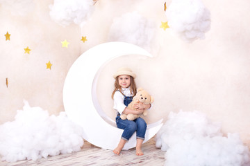 Sweet Dreams. Little cute girl sitting on the moon with clouds and stars with a teddy bear in their hands and playing. Little astrologer. Little traveler. Children's room decor in a fabulous style.