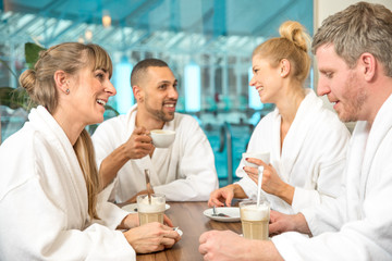junge Leute Gruppe trinken Kaffee, Cappuccino und Sekt in einer Wellnesslandschaft Schwimmbad. Sie tragen einen weißen Bademantel in der Sauna