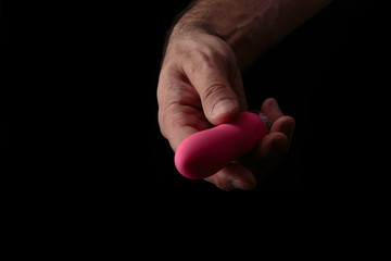 Pink vibrator in male hand on black background with artistic light