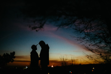 Fototapeta premium silhouette of happy couple looking at each other and touching with gentle on background of sunset sky and city lights