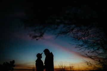 Fototapeta na wymiar silhouette of happy couple looking at each other and touching with gentle on background of sunset sky and city lights