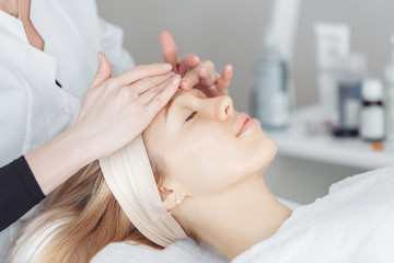 Unknown masseuse beautician doing a face massage to her client a beautiful young woman. Skin care concept