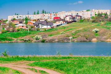 Fototapeta premium Green and bright, spring landscape. View of the city and the mountain from the field of flowering trees and young foliage. Juicy fresh grass and vegetation. Rostov region, Russia.