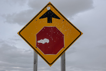 Red road stop sign full of bullet holes