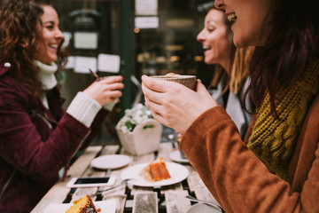 A woman is holding a cup of coffee between her hands. She is enjoying talking with her friends in a nice sunny day. Selective focus. Lifestyle