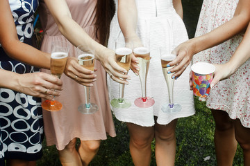 hands of woman holding colorful glasses and toasting champagne at joyful party in summer park, bridal shower or wedding reception