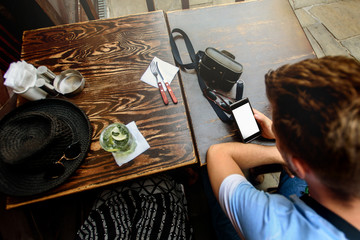 traveler man holding phone with empty screen on wooden table with tasty mojito and photo camera, summer vacation concept