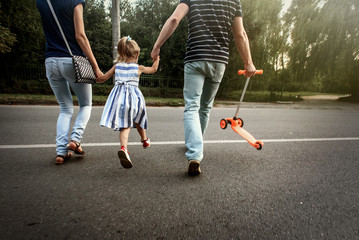 happy stylish parents holding hands with daughter and walking in sunny  street, tender family moment