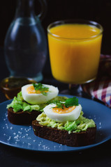 Healthy healthy snack (breakfast) - a sandwich with avocado and egg on a gray plate and a glass of fresh orange juice.