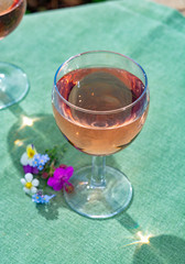 Glass with cold rose wine and wild flowers in summer sunny day