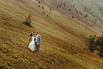 gorgeous bride and stylish groom hugging at sunny landscape,  boho wedding couple, luxury ceremony at mountains with amazing view, space for text