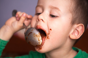 Close up portrait of Cute little boy eating chocolate yogurt at breakfast. Face messy with...