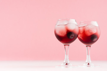 Modern refreshing alcohol red drinks in wineglasses with ice cubes, blueberry on white wood board and pastel pink background, copy space.
