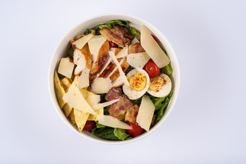 Selective focus Caesar salad with roasted chiken, bacon, quail eggs, lettuce leaves, chips, parmesan, cherry tomatoes on the white round plate close up