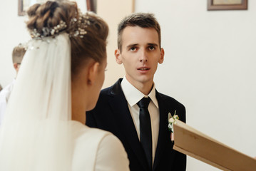 happy stylish bride and elegant groom exchanging vows at catholic wedding ceremony at church