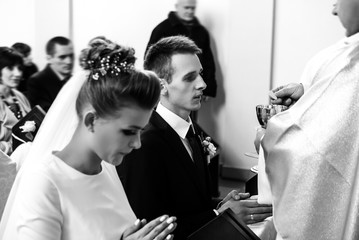 bride and groom having communion with priest on knees at wedding ceremony in church