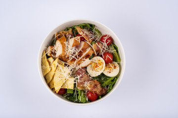 Selective focus Caesar salad with roasted chiken, bacon, quail eggs, lettuce leaves, chips, parmesan, cherry tomatoes on the white round plate close up