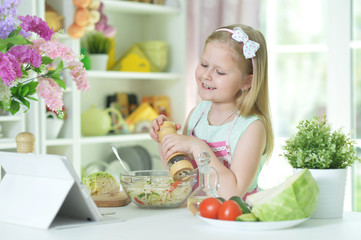 Cute little girl spicing salad on kitchen table