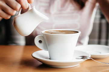 Americano coffee. Girl pours milk into a cup of americano coffee. Coffee with milk