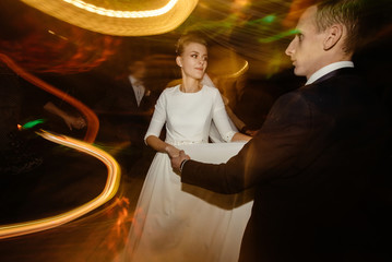 gorgeous bride and stylish groom emotionally dancing, luxury wedding reception in restaurant, cool motion light