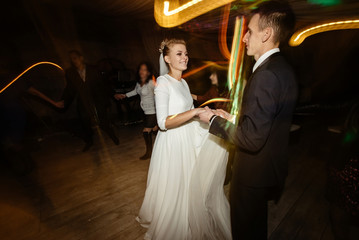 gorgeous bride and stylish groom emotionally dancing, luxury wedding reception in restaurant, cool motion light