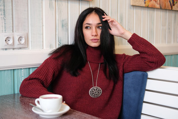 Closeup portrait of young attractive woman in red warm knitted sweater sitting in a cafe. Woman drinking hibiscus tea in the restaurant.