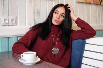 Closeup portrait of young attractive woman in red warm knitted sweater sitting in a cafe. Woman drinking hibiscus tea in the restaurant.