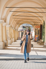 young pretty fashionable woman walking in brown coat by street