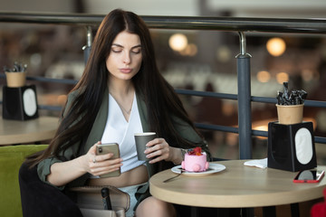 Young businesswoman with cell telephone in hand thinking about something serious while sitting in modern cafe interior. 