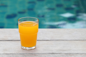 Glass of orange juice placed on a wooden floor by the pool.