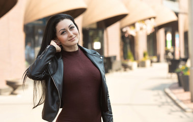 Obraz premium Amazing joyful pretty girl with long brunette hair posing outdoor. Leather jacket, brunette hair. Fashion street stile portrait. 