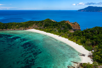 Aerial drone view of a lush, green tropical island with sandy beach