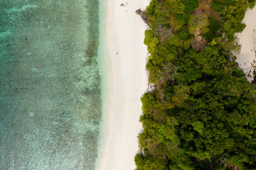 Aerial drone view of a lush, green tropical island with sandy beach