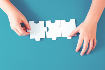 Jigsaw puzzle piece in one hand and another hand on the blue desk, top view. Teamwork and creativity solution or idea concept with copy space on trendy ocean blue background
