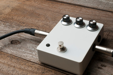 A blank white guitar pedal with vintage knobs and plugged jacks on the floor