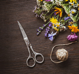 Wild flowers and scissors on old grunge wooden background (chamomile lupine dandelions thyme mint bells rape)